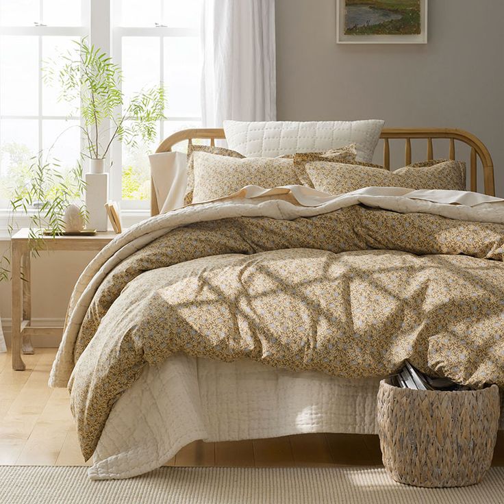 a bed in a bedroom next to a window with white drapes and plants on the windowsill