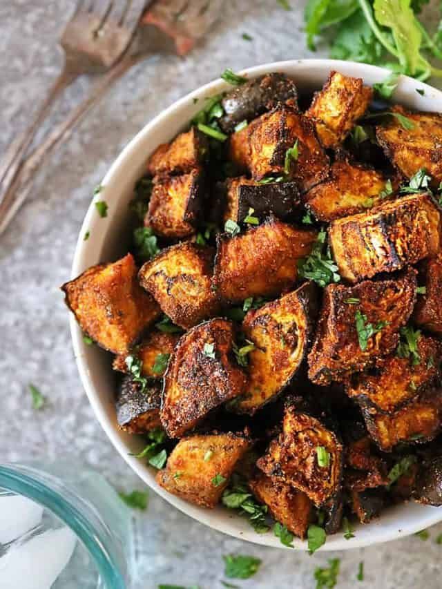 a white bowl filled with cooked potatoes and parsley on top of a table next to a fork