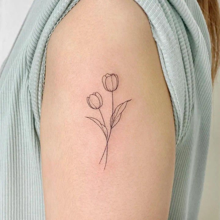 a woman's arm with a single flower tattoo on the left side of her shoulder