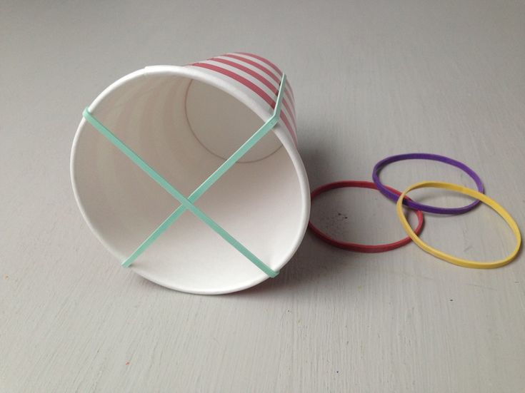 a paper cup with colored bands around it on a white surface, next to some rings