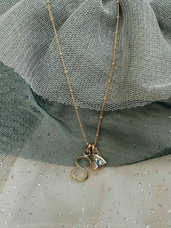 a gold necklace with an initial charm on it and a diamond pendant hanging from the bottom