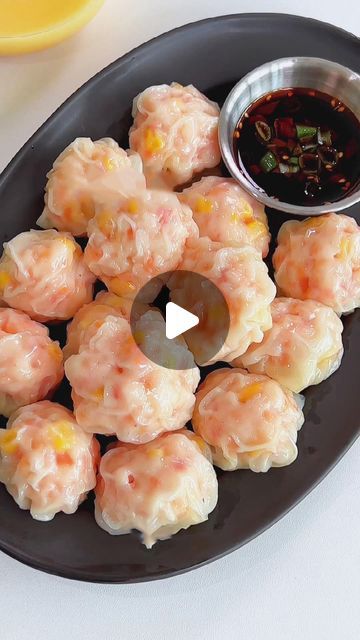 a black plate topped with dumplings next to a bowl of dipping sauce on top of a white table