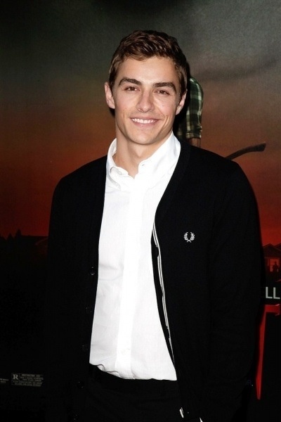 a young man in a white shirt and black blazer smiles at the camera while standing next to a movie poster