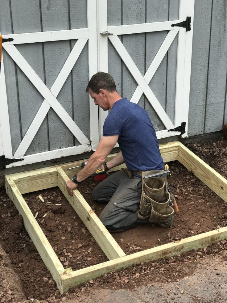 a man kneeling down in the dirt working on a wooden frame with an electric drill