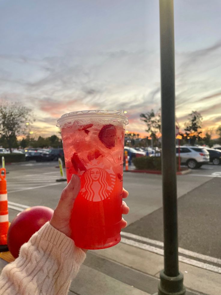 a person holding up a starbucks drink in front of a parking lot