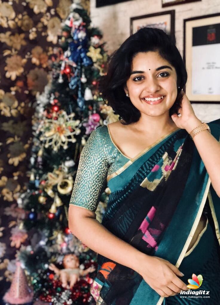 a woman standing in front of a christmas tree wearing a sari and smiling at the camera