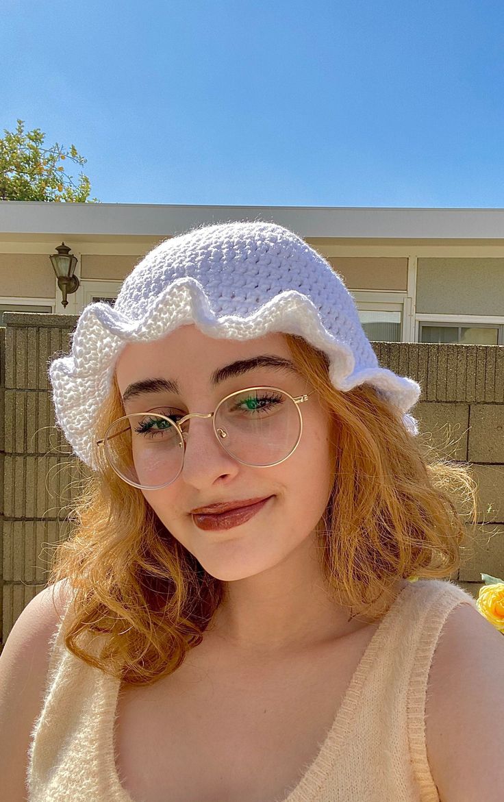 a young woman wearing glasses and a white crocheted hat is posing for the camera