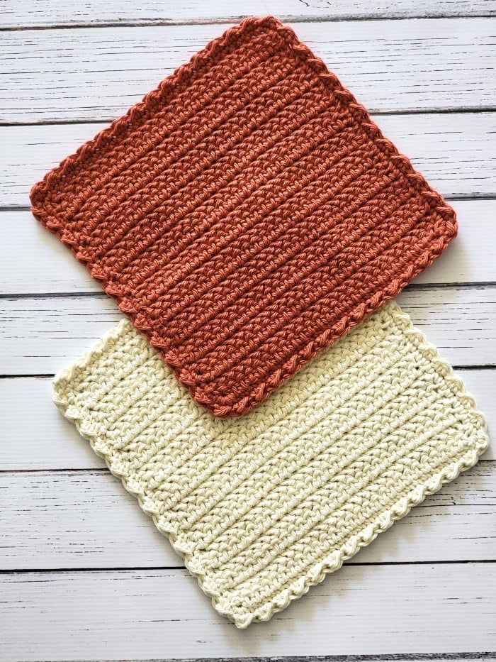 two crocheted dishcloths sitting next to each other on a white wooden surface