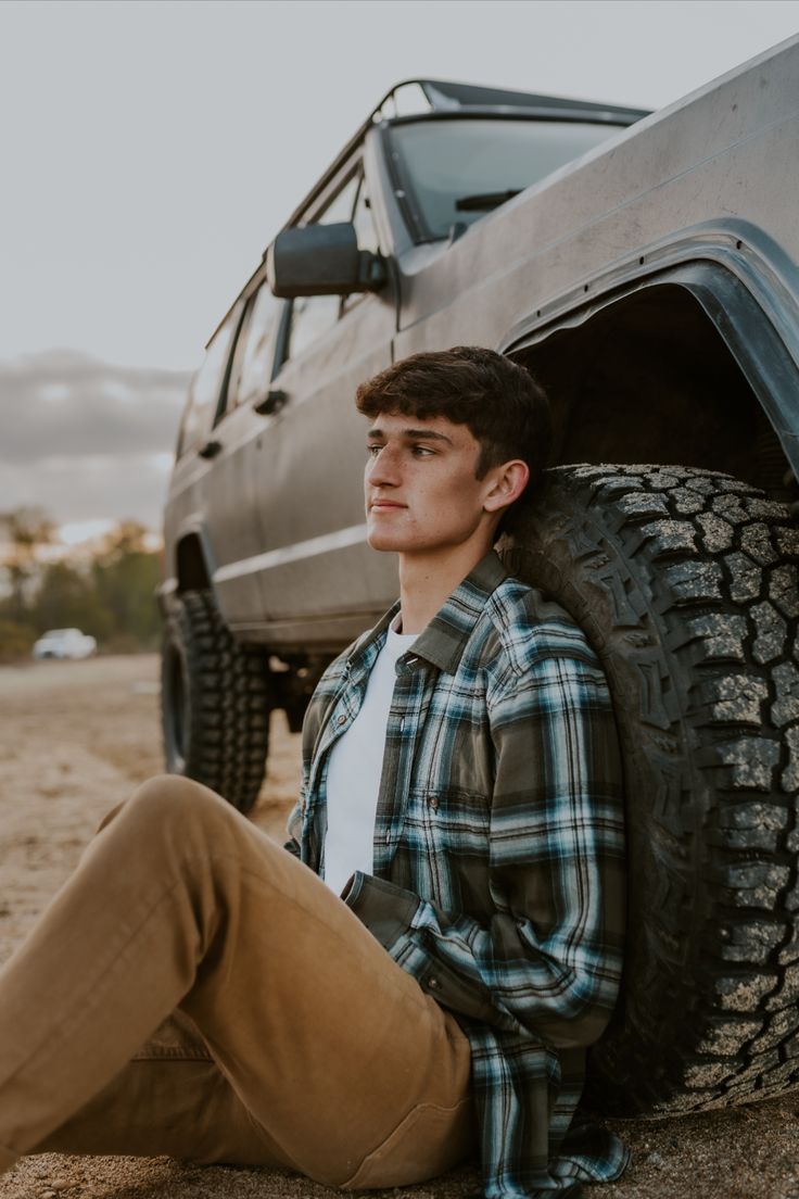 a young man sitting on the ground in front of a truck with his feet up