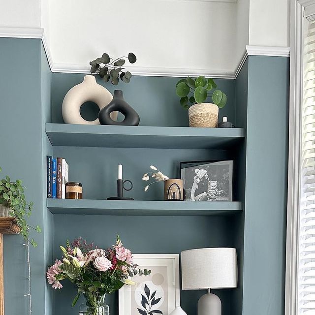 a living room with blue walls and shelves filled with vases, flowers and pictures