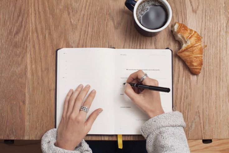 a person writing on a notebook with a croissant and coffee