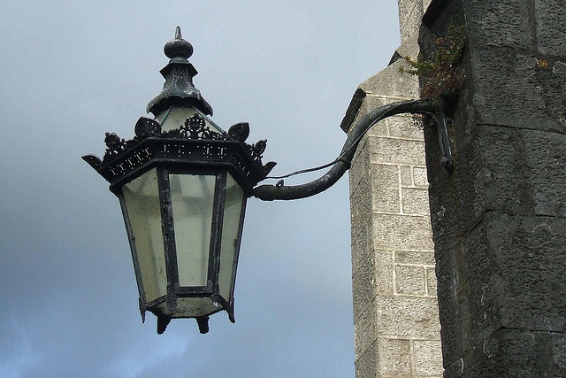 an old fashioned street light hanging off the side of a stone building on a cloudy day