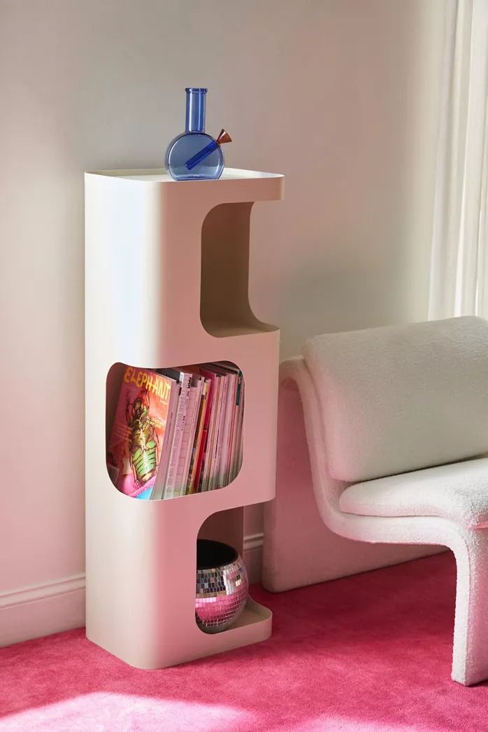 a white chair sitting next to a shelf with books on top of it in a pink room