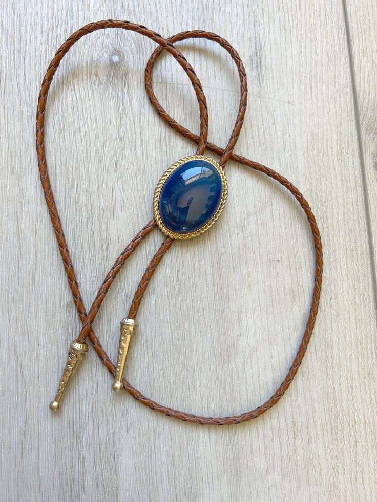 This awesome bolo tie has a southwestern design and blue agate centerpiece. Each of our stones is unique . The cord is genuine brown leather. It has a gold metal frame and matching gold tips. Our bolos pair nicely with many of our belt buckles! They make wonderful gifts. The western bolo tie rope length is 100cm(39") ; charm agate stone pendant size is 5*4cm(1.97*1.57in) Western Style Brown Jewelry With Adjustable Length, Bohemian Blue Bolo Ties As Gift, Brown Western Jewelry With Adjustable Length, Adjustable Western Gold Jewelry, Adjustable Gold Western Jewelry, Brown Western Jewelry With Adjustable Cord, Blue Adjustable Hand Tooled Jewelry, Adjustable Southwestern Gold Jewelry, Adjustable Hand Tooled Blue Jewelry