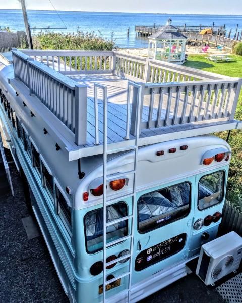 a blue and white bus parked in front of the ocean with a ladder on it's side