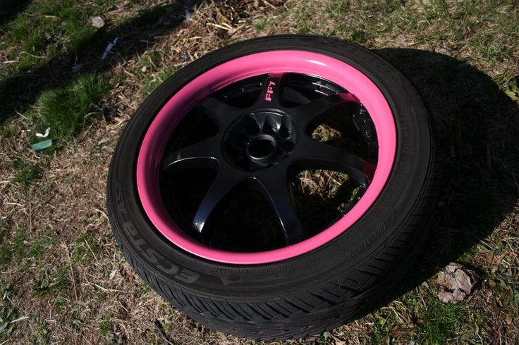 a pink rim and black spokes sit on the grass next to a tire that is laying on the ground