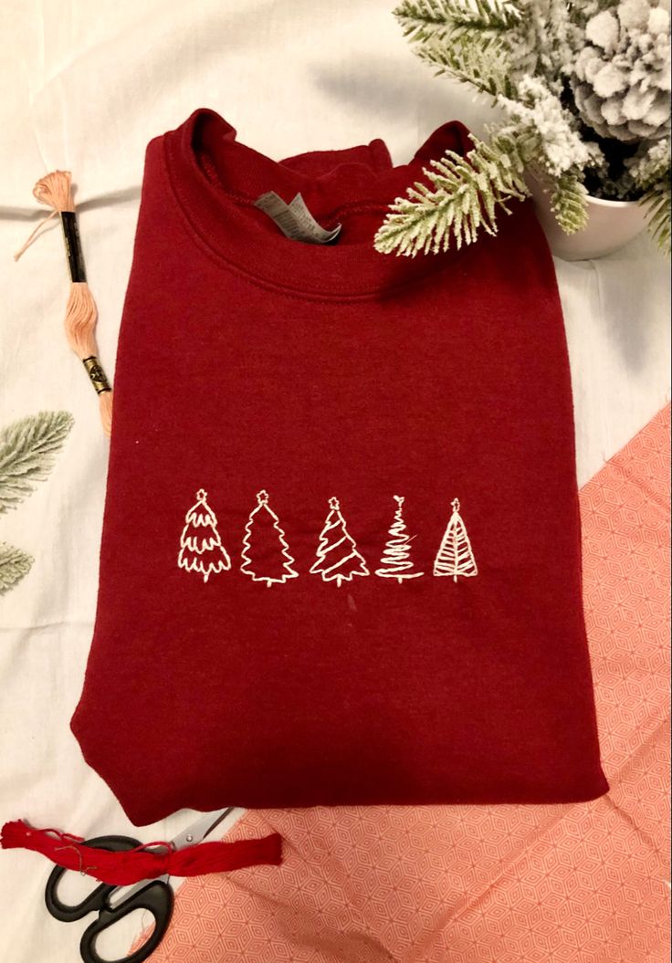 a red shirt with white trees on it next to scissors and some pine branches in the background