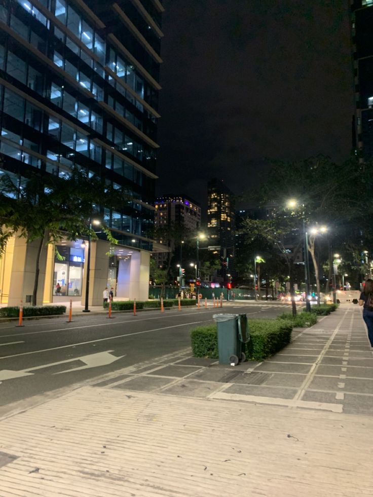 an empty city street at night with people walking on the sidewalk and buildings in the background