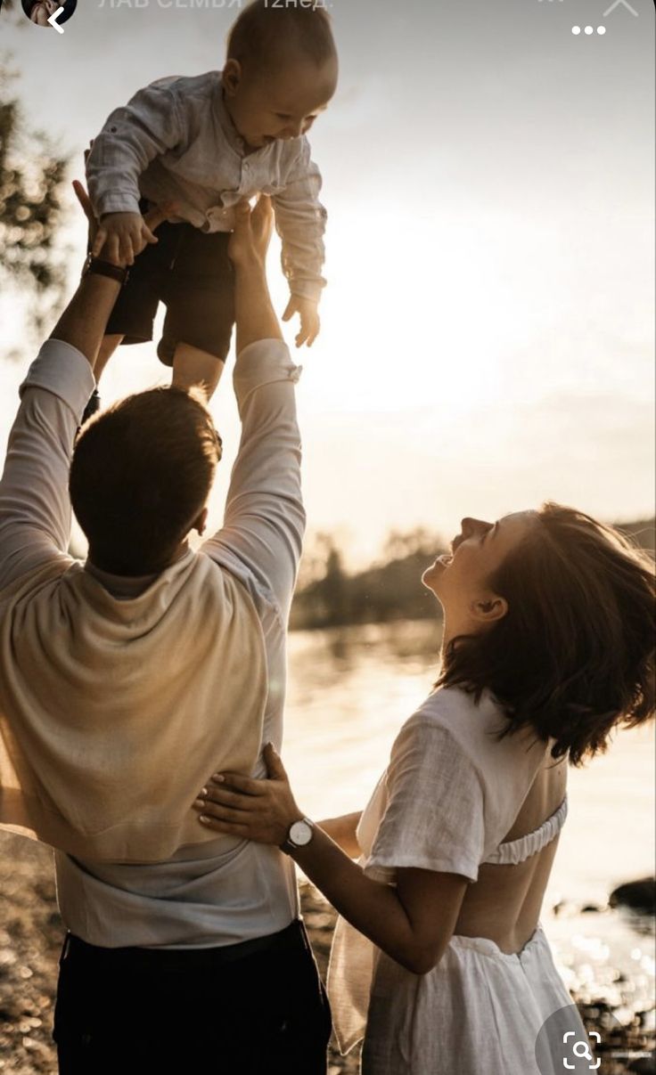 a man holding a baby up in the air while standing next to two other people