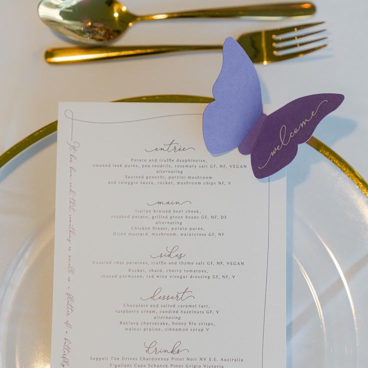 a white plate topped with a purple butterfly next to a silver fork and paper menu