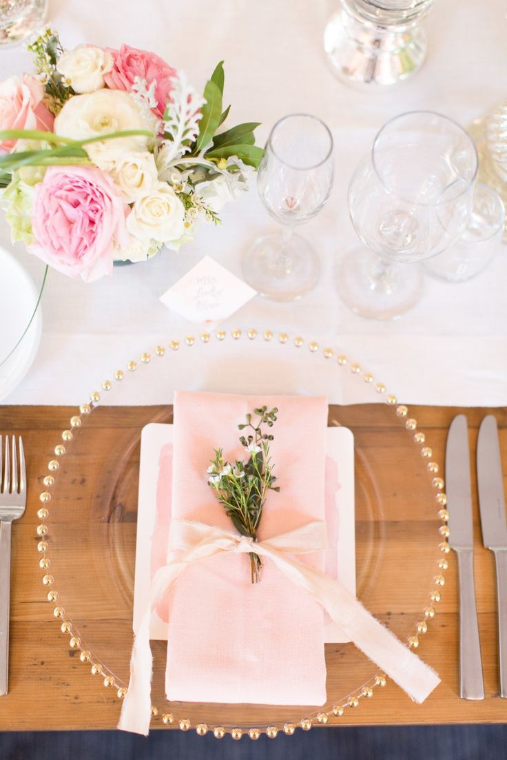 a place setting with pink napkins, silverware and flowers