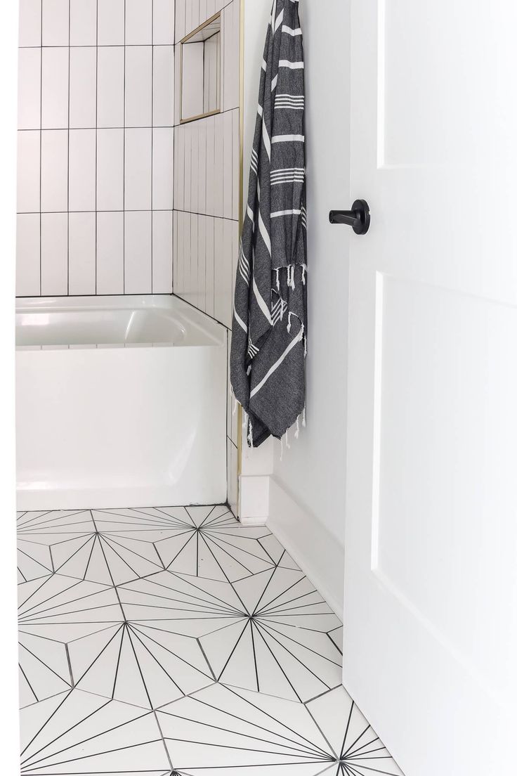 a white bathroom with black and white tiles on the floor next to a bathtub