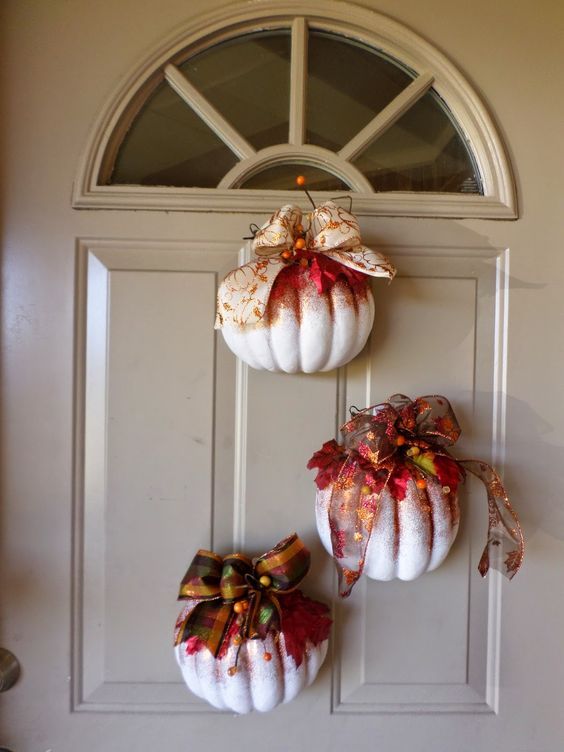 three white pumpkins with bows hanging from the front door