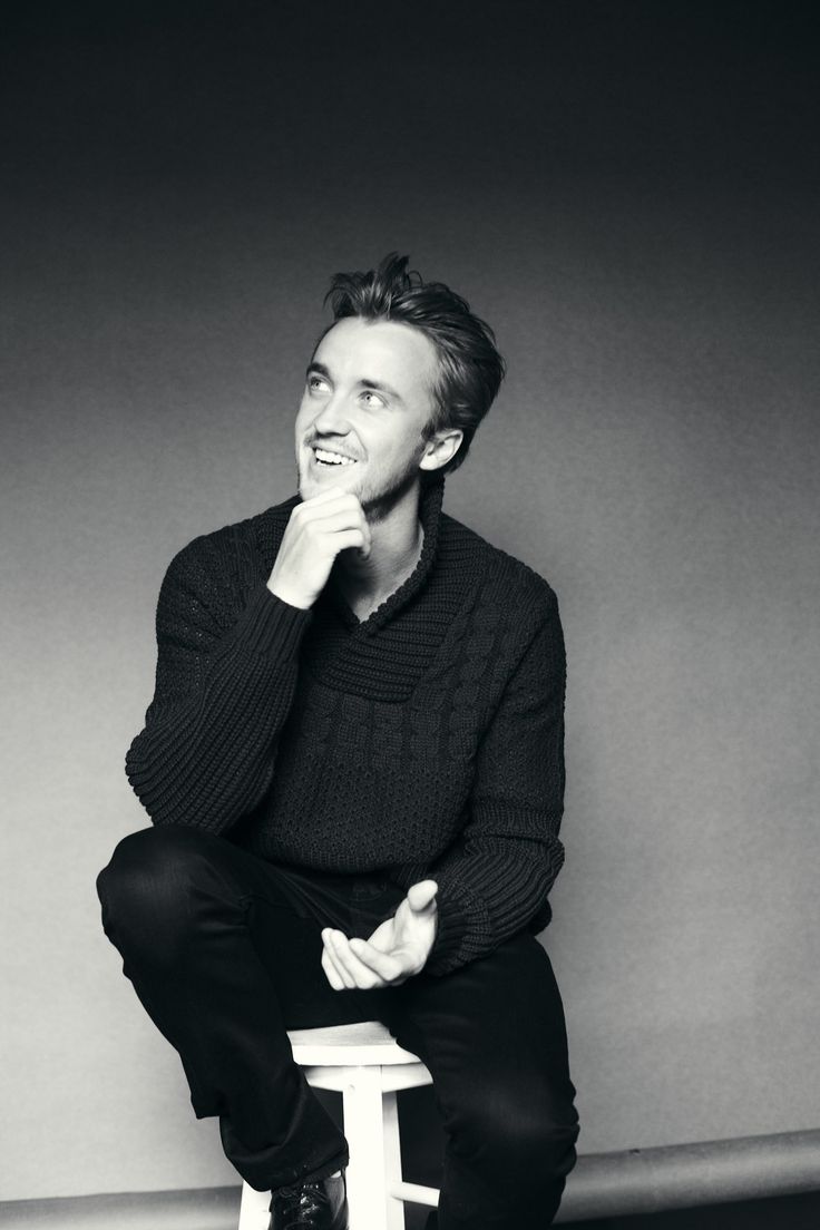 a black and white photo of a man sitting on a stool with his hands in his mouth