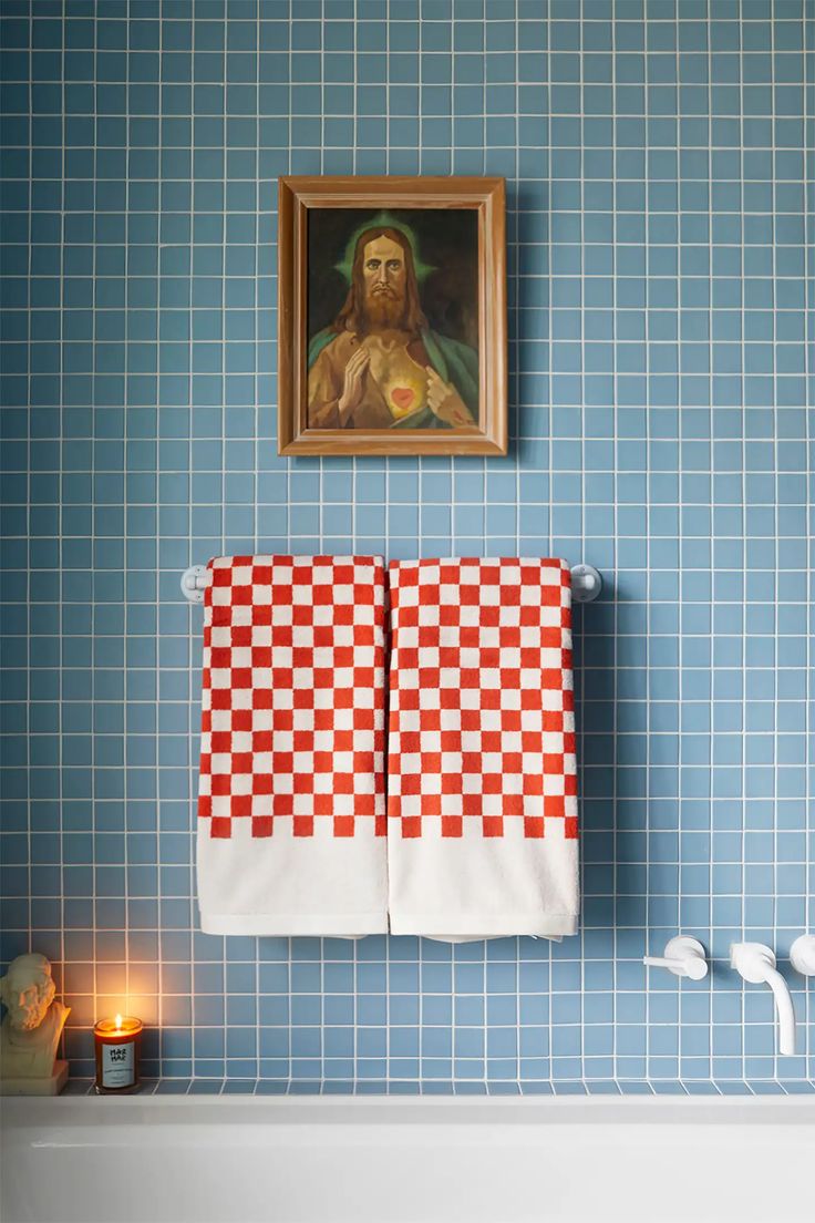 two towels are hanging on the wall next to a painting and candles in a bathroom