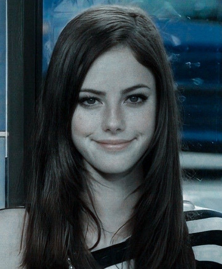 a woman with long brown hair wearing a black and white striped shirt smiling at the camera