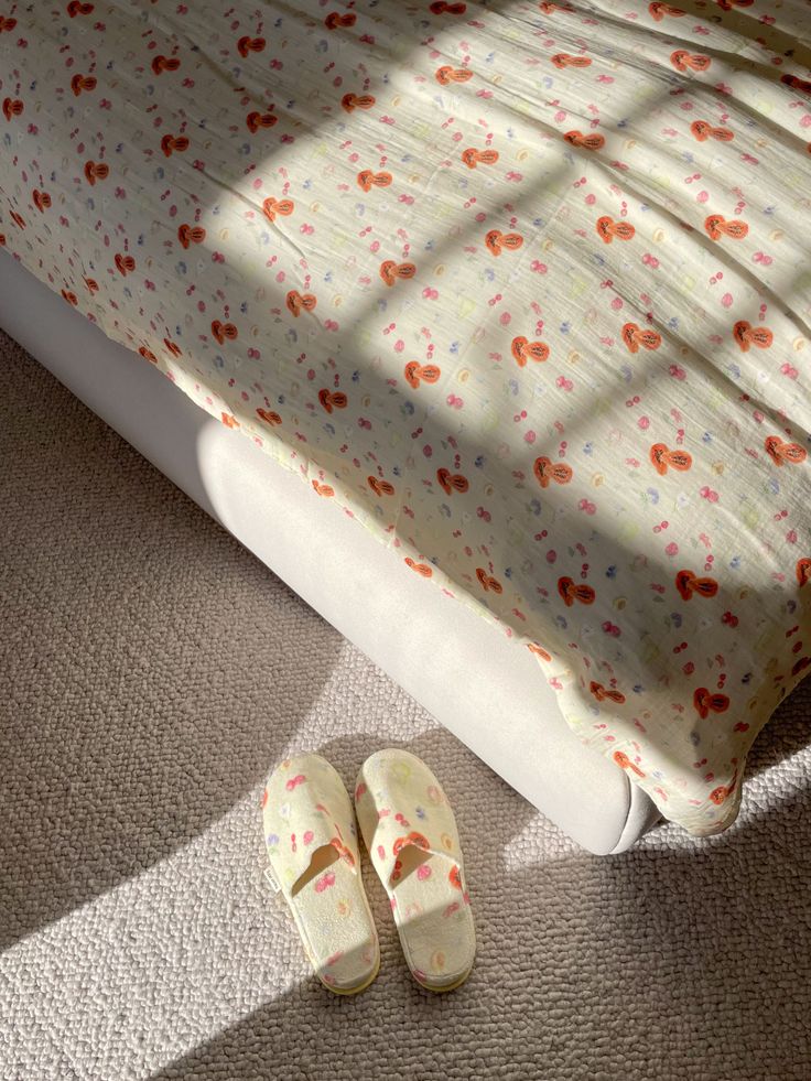 two slippers are laying on the floor next to a bed with a floral bedspread