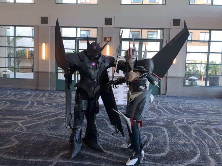 two people in costumes standing next to each other on the floor with windows behind them