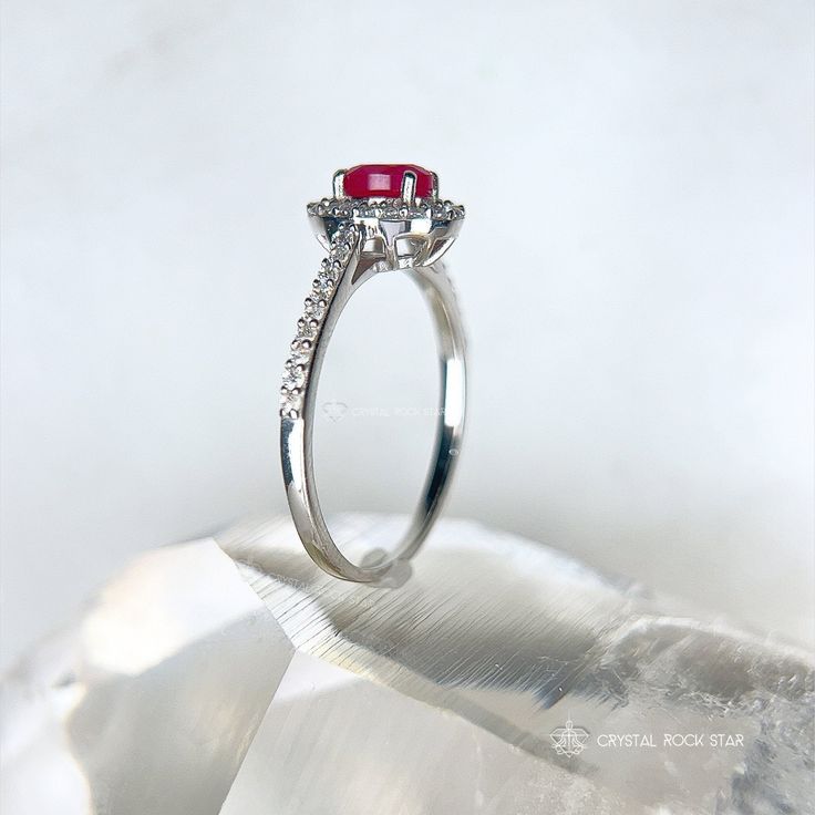 Genuine Ruby Oval Faceted Halo Sterling Silver Ring Add this beautiful pink Ruby halo ring and elevate your jewelry collection. This ring boasts an oval cut natural Ruby gemstone that exudes elegance and sophistication. The accented halo twinkles around the opaque Ruby, while the pave band will take your breath away with its sparkling accent stones. Whether you're treating yourself or looking for the perfect gift for a loved one, this Ruby ring is a beautiful choice for someone looking for a memorable design. Makes a stunning gift for a July birthday recipient as Ruby is the July birthstone. Ruby is considered a stone of love and vitality. Ruby is part of the Corundum crystal family and gets its beautiful pink tones from trace mineral elements of chromium. Sizes Available: 5, 7, 8, 9 DIMEN Fine Jewelry Ruby Ring With Halo, Pink Ruby Ring With Halo Design, Oval Ruby Halo Ring Fine Jewelry, White Gold Ruby Ring With Halo, Round Ruby Ring With Halo Setting For Proposal, Oval Ruby Ring With Diamond Halo, Oval Halo Ring With Accent Stones For Promise, Diamond Halo Ring With Gemstone In Round Band, Oval Halo Diamond Ring Fine Jewelry