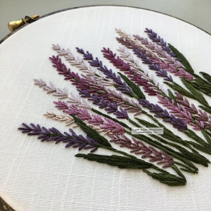 a close up of a embroidery on a white cloth with purple and green flowers in it