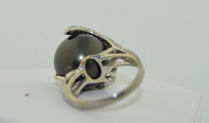 This is an impressively large pearl ring. The pearl is a south Sea Black Tahitian Pearl. The pearl is drilled and mounted with pave diamond accents. The small prong is drilled on the side and the fingers of diamonds are securing the pearl with no movement. This pearl is big, measuring in at 15.5 mm. It is a deep grey/black, perfectly round. There are a couple of natural dimples on the side not the top of the pearl as photographed The setting is 14K White gold, not hallmarked but tested and guara Elegant Round Cabochon Pearl Ring, Anniversary Black Tahitian Pearl Ring, Formal Black Tahitian Pearl Ring, Black Tahitian Pearl Ring, Luxury Tahitian Pearl Ring For Formal Occasions, Elegant Tahitian Pearl Ring Gift, Tahitian Pearl Ring With Diamond Accents For Wedding, Tahitian Pearl Ring With Diamond Accents Fine Jewelry, Fine Jewelry Tahitian Pearl Ring With Diamond Accents