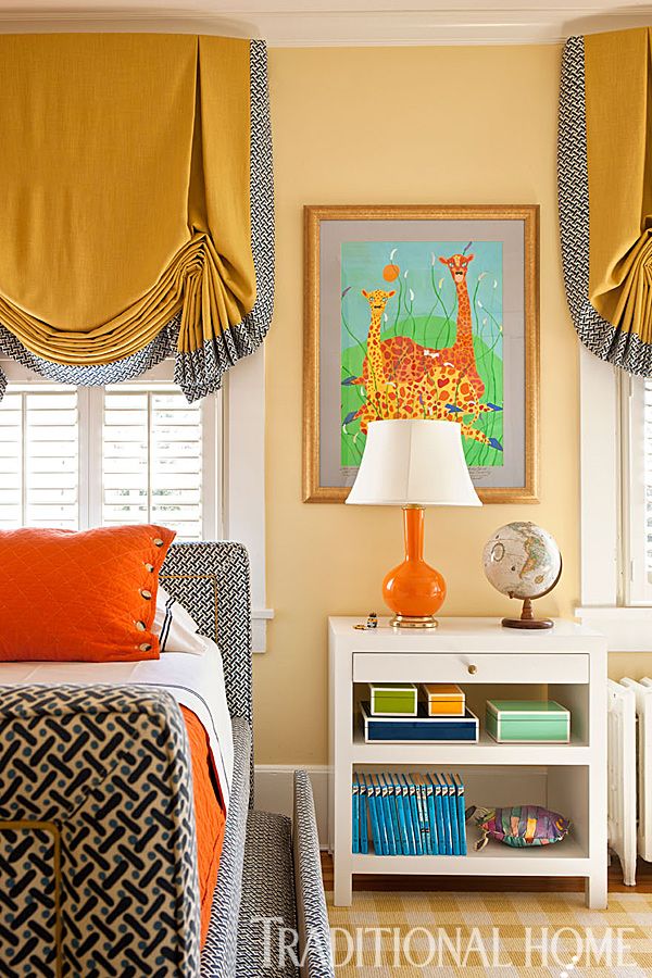 a bedroom with yellow walls and curtains, a white bed topped with an orange pillow next to a painting on the wall