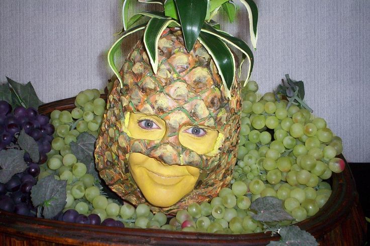 a pineapple with a face made out of it surrounded by grapes and other fruit