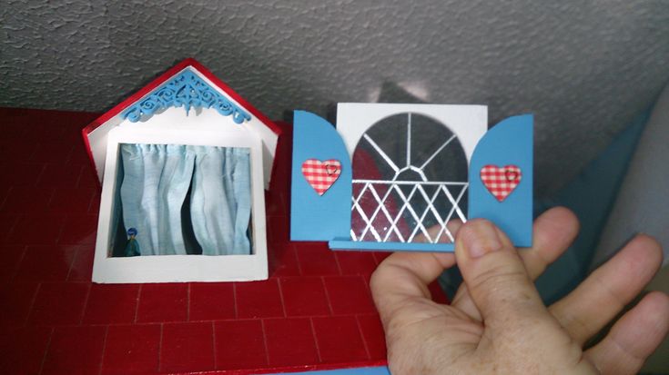 a hand is holding a small card with a window and curtains in the box next to it