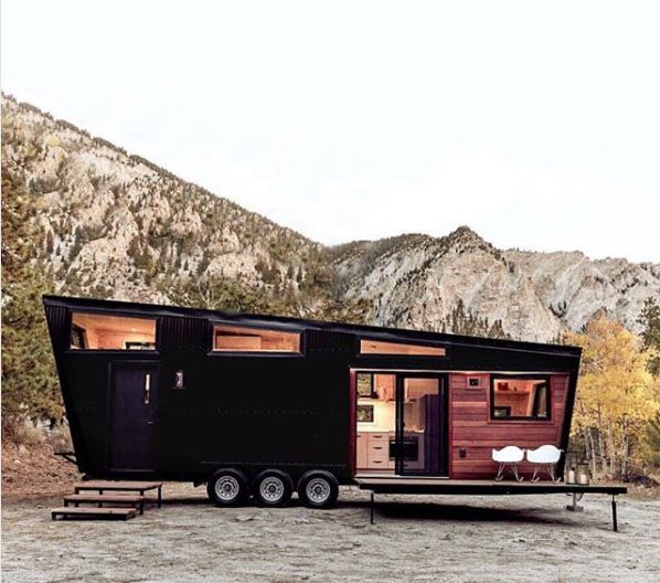 a tiny house on wheels is parked in front of a rocky mountain range with mountains behind it