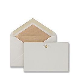 a white envelope with a gold bee on the front and bottom, sitting next to an envelope