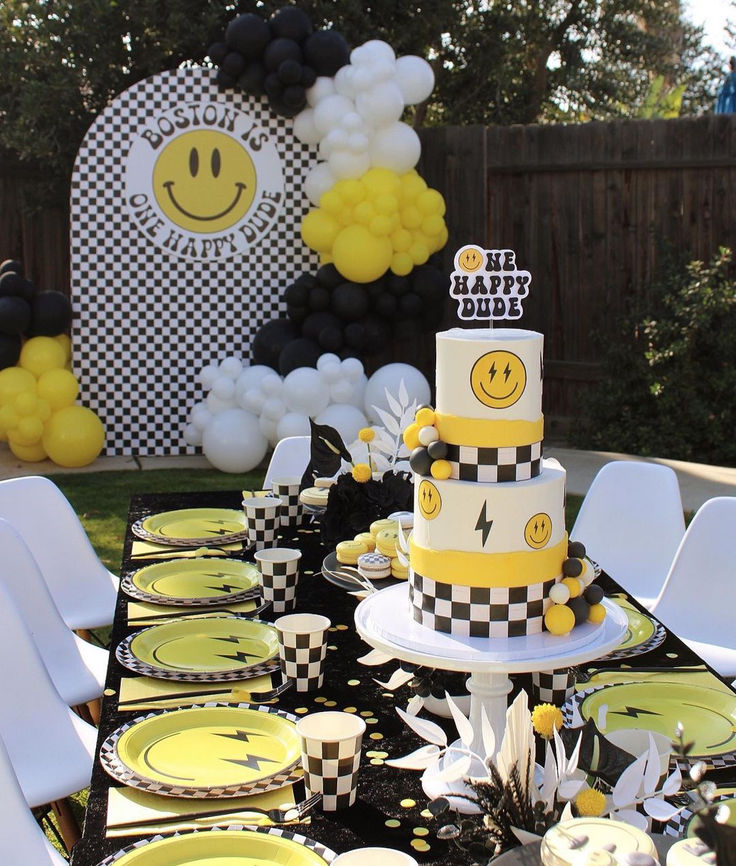 a black and white table topped with yellow and white desserts next to balloons in the shape of smiley faces