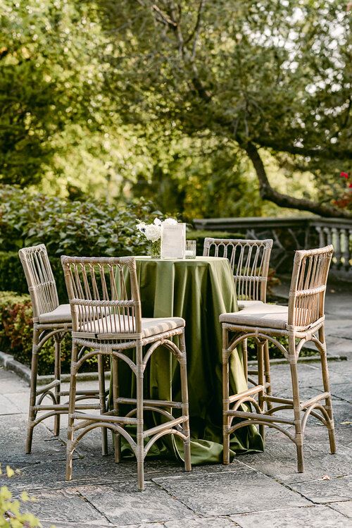 the table is set with four chairs and a green tablecloth on it, in front of some trees