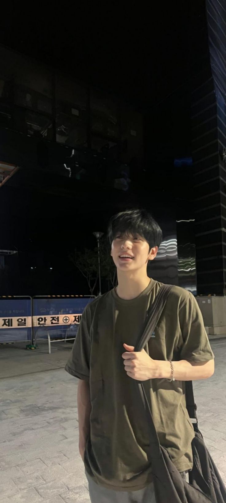 a young man standing in front of a tall building at night with his hand on his hip