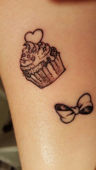 a cupcake with a bow tattoo on the side of her neck is shown in black ink