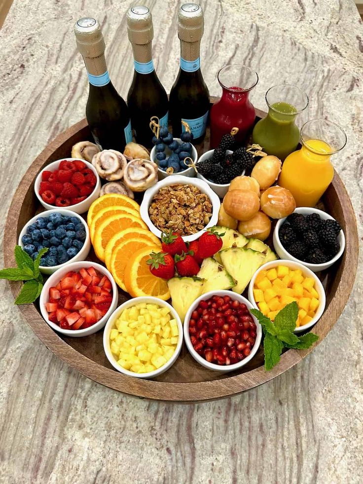 a wooden tray filled with different types of fruits and vegetables next to bottles of wine