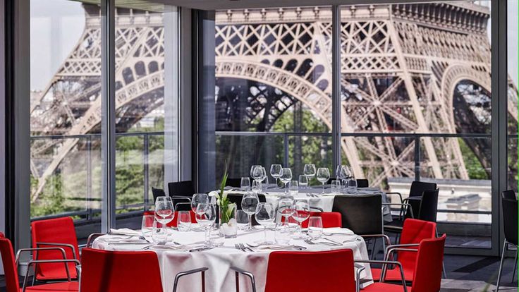 a dining room with red chairs and tables in front of the eiffel tower