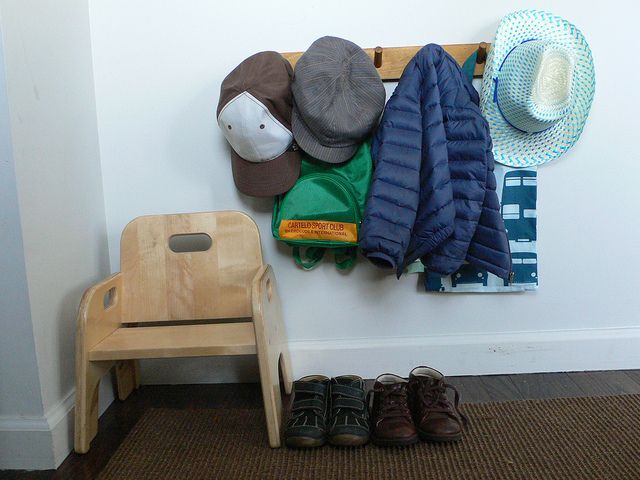 hats and coats are hanging on the wall next to a wooden bench with two pairs of shoes