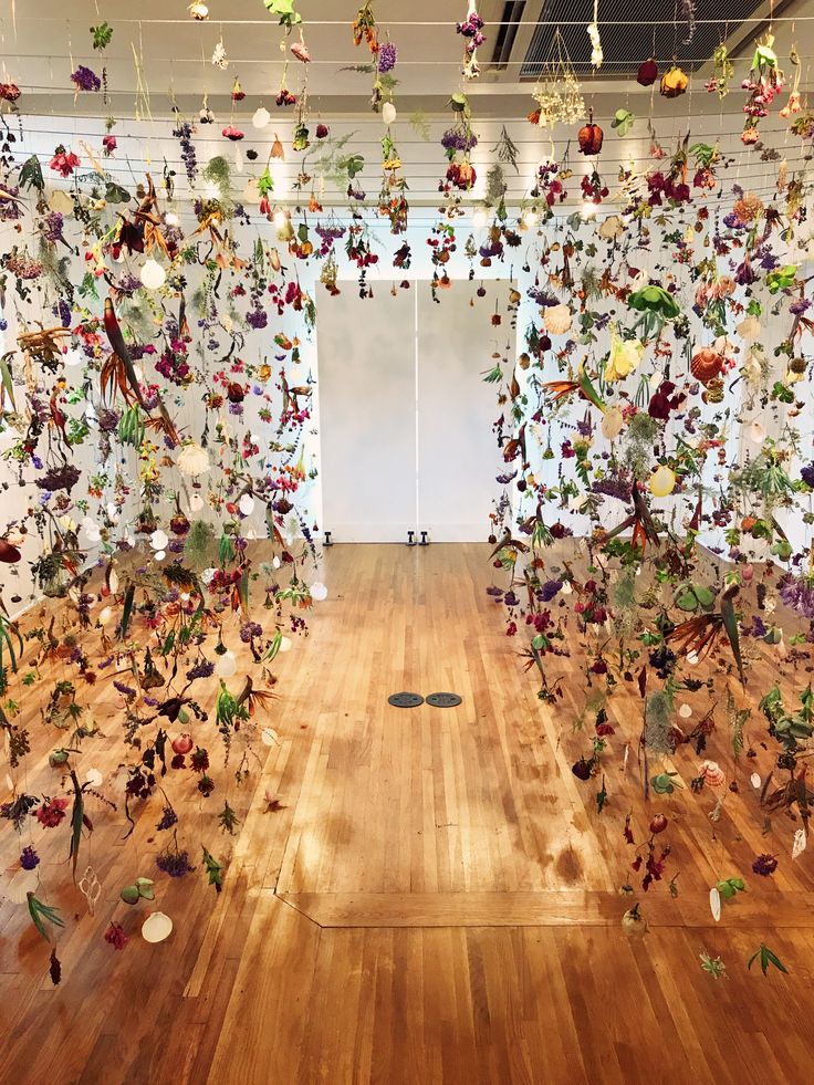 a room filled with lots of different types of flowers hanging from the ceiling and wooden floors