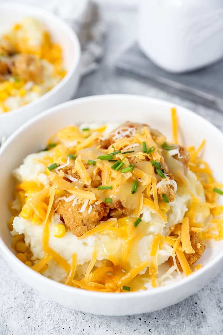 two white bowls filled with mashed potatoes topped with cheese and green onions on a table