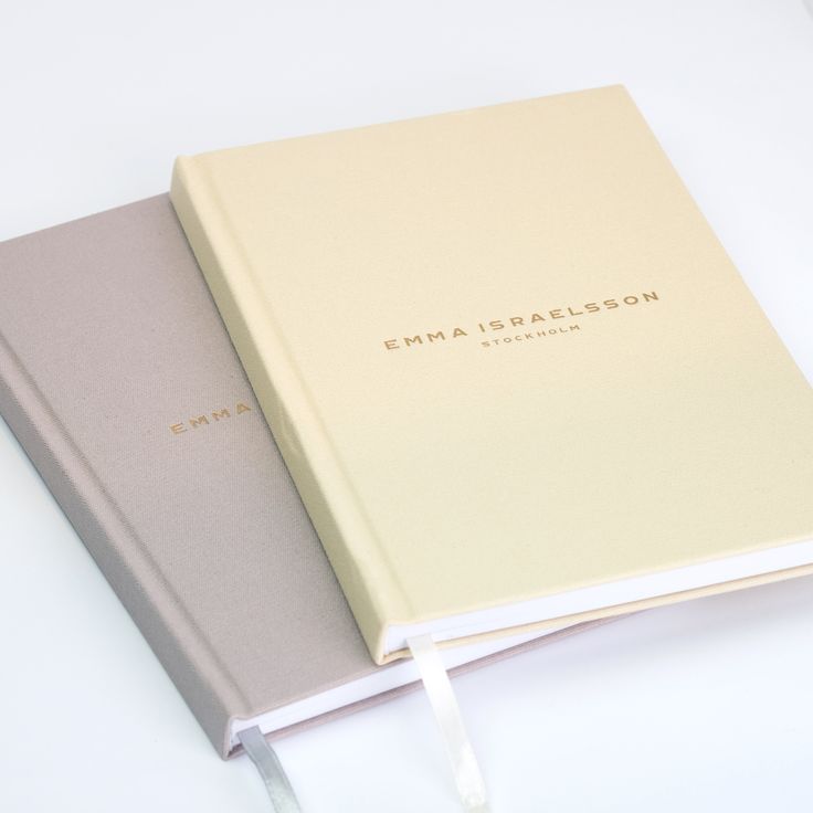 two notebooks sitting next to each other on top of a white table with ribbon